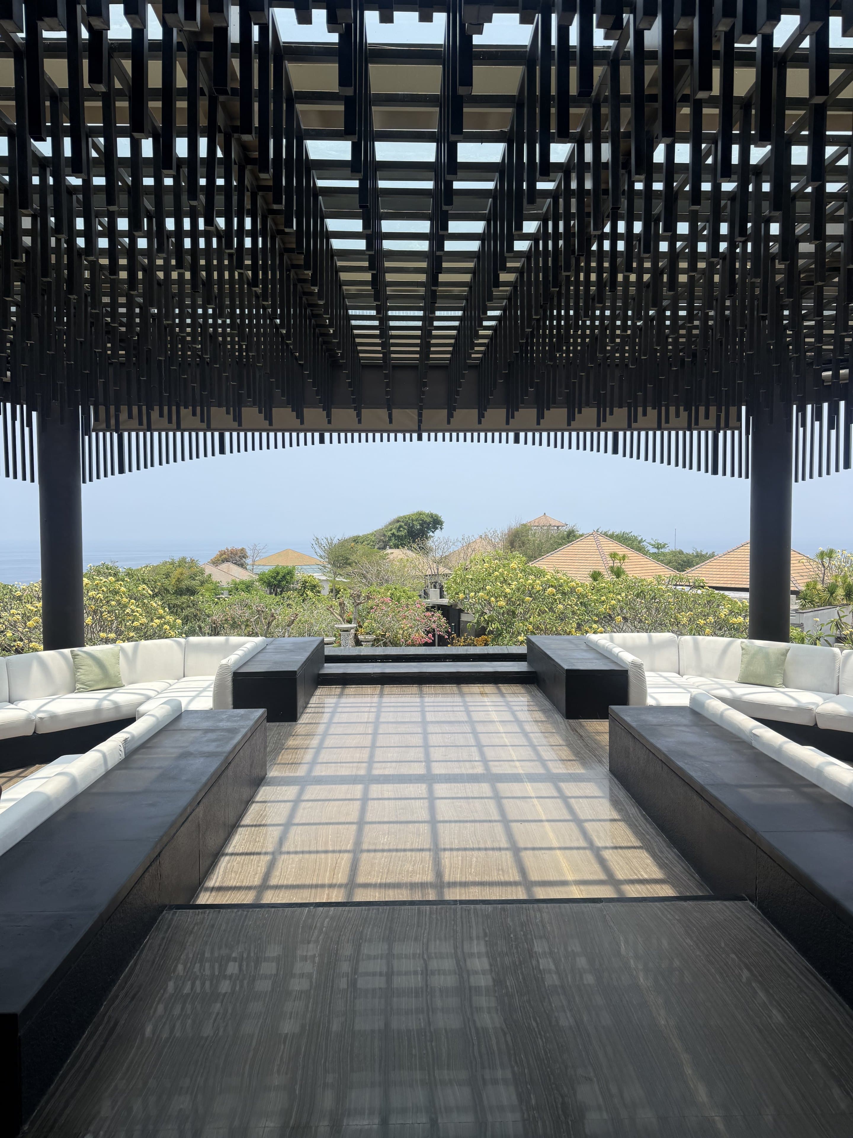 Open-air lounge with white sofas under a timber pergola, looking out to the ocean