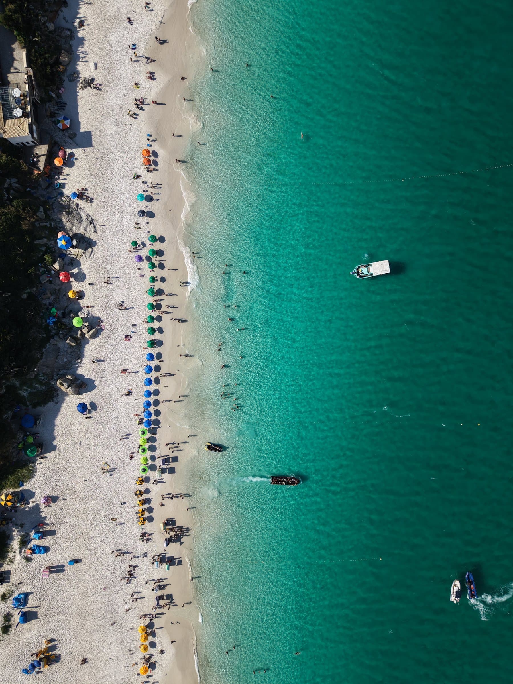 Top-down view of beach umbrellas along white sand and turquoise water, boats offshore