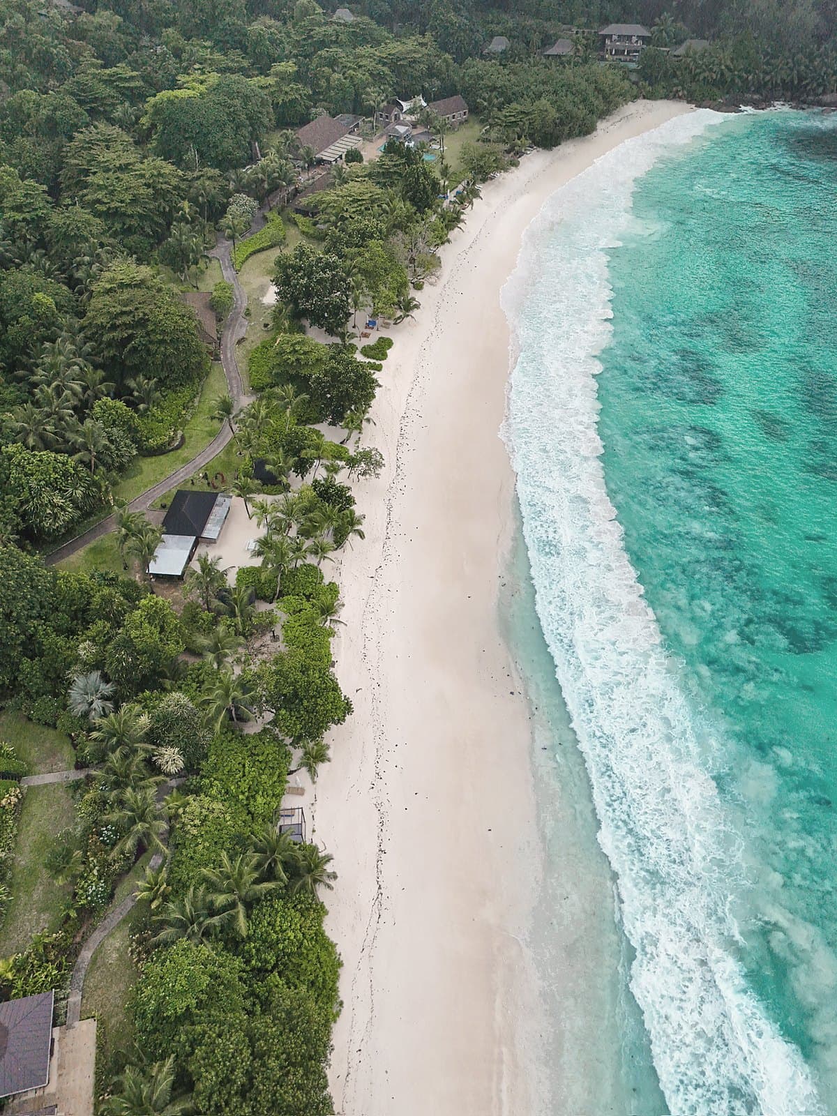 Drone view of a long white beach curving past jungle, surf breaking on the reef