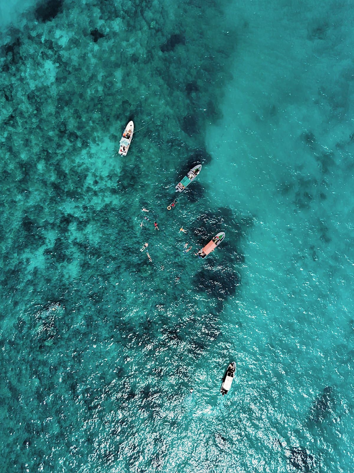 Small boats floating over a turquoise reef seen from directly above