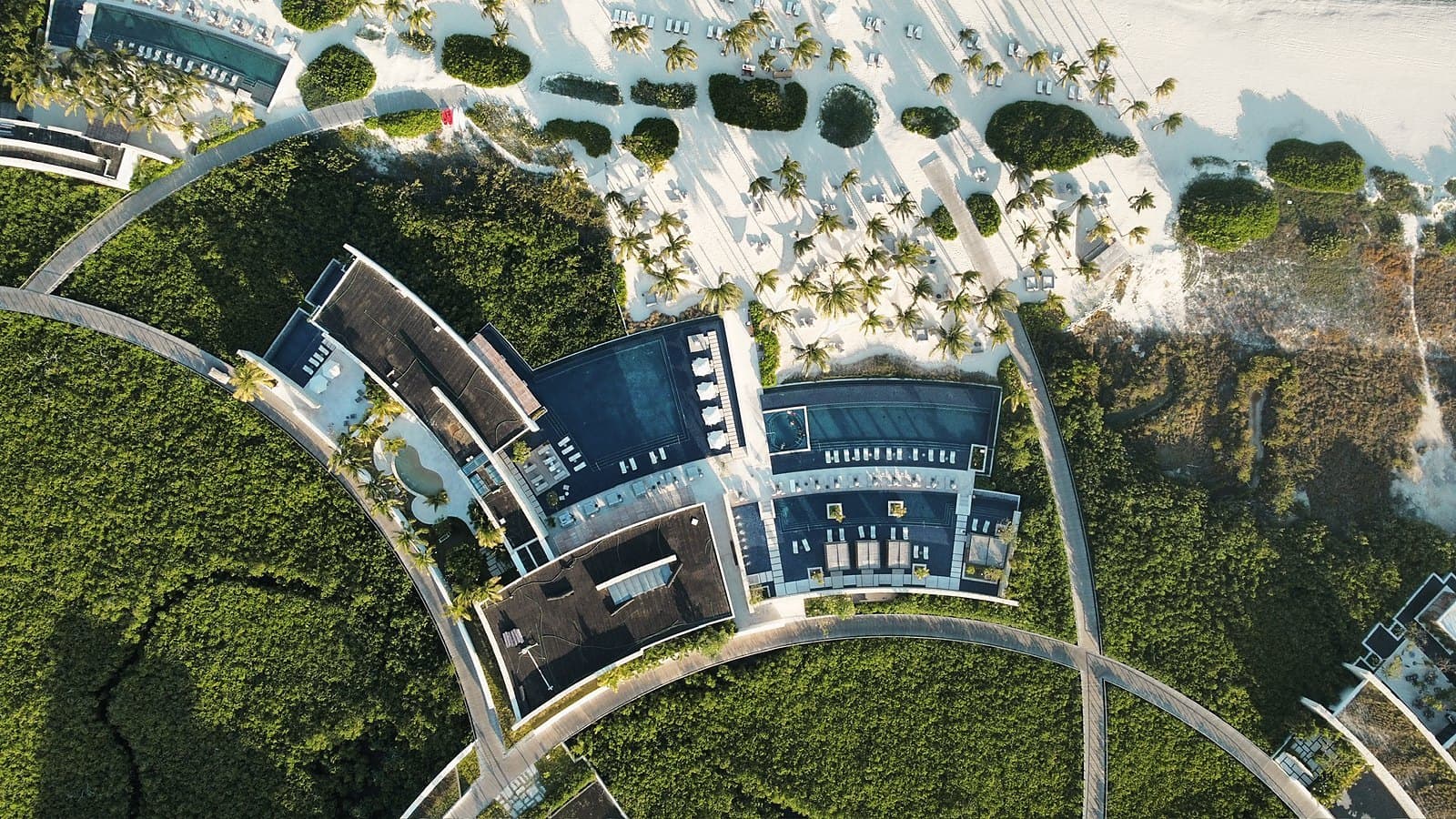 Drone view straight down on curved green roofs, pool decks and a white beach