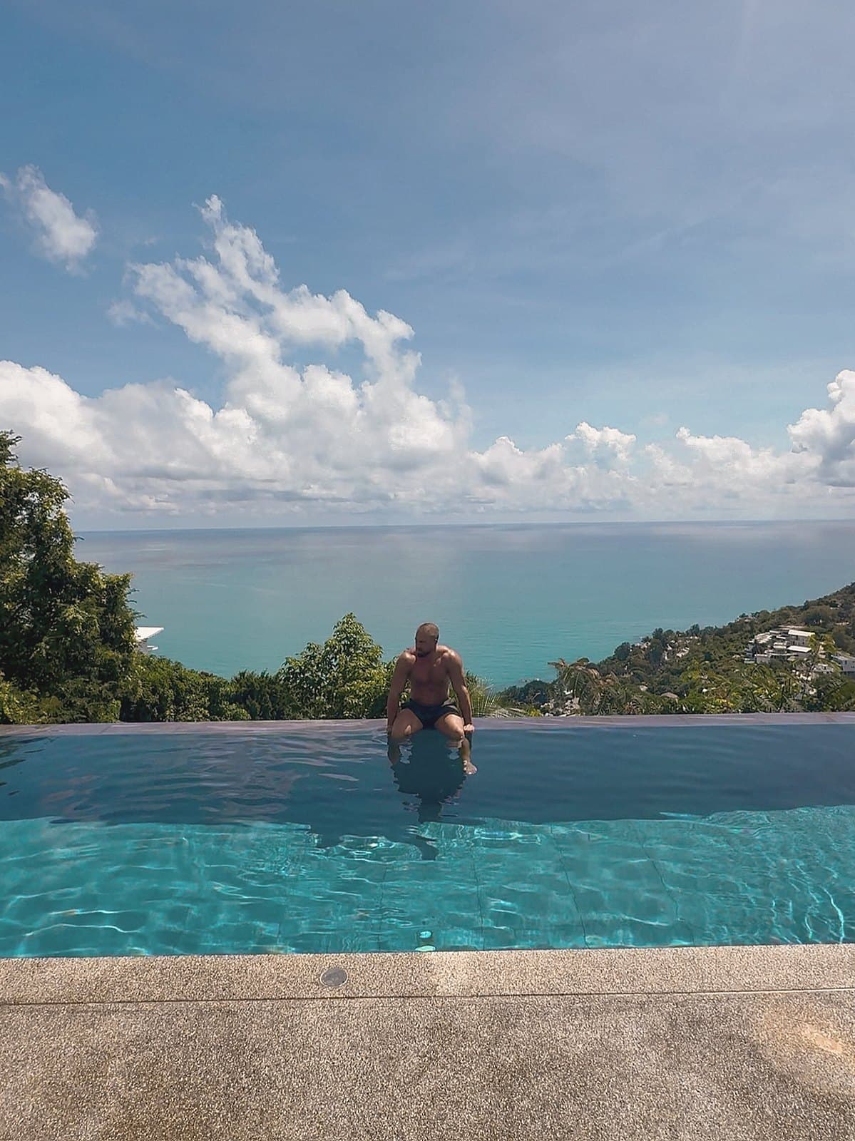 Figure resting at the edge of an infinity pool facing the sea
