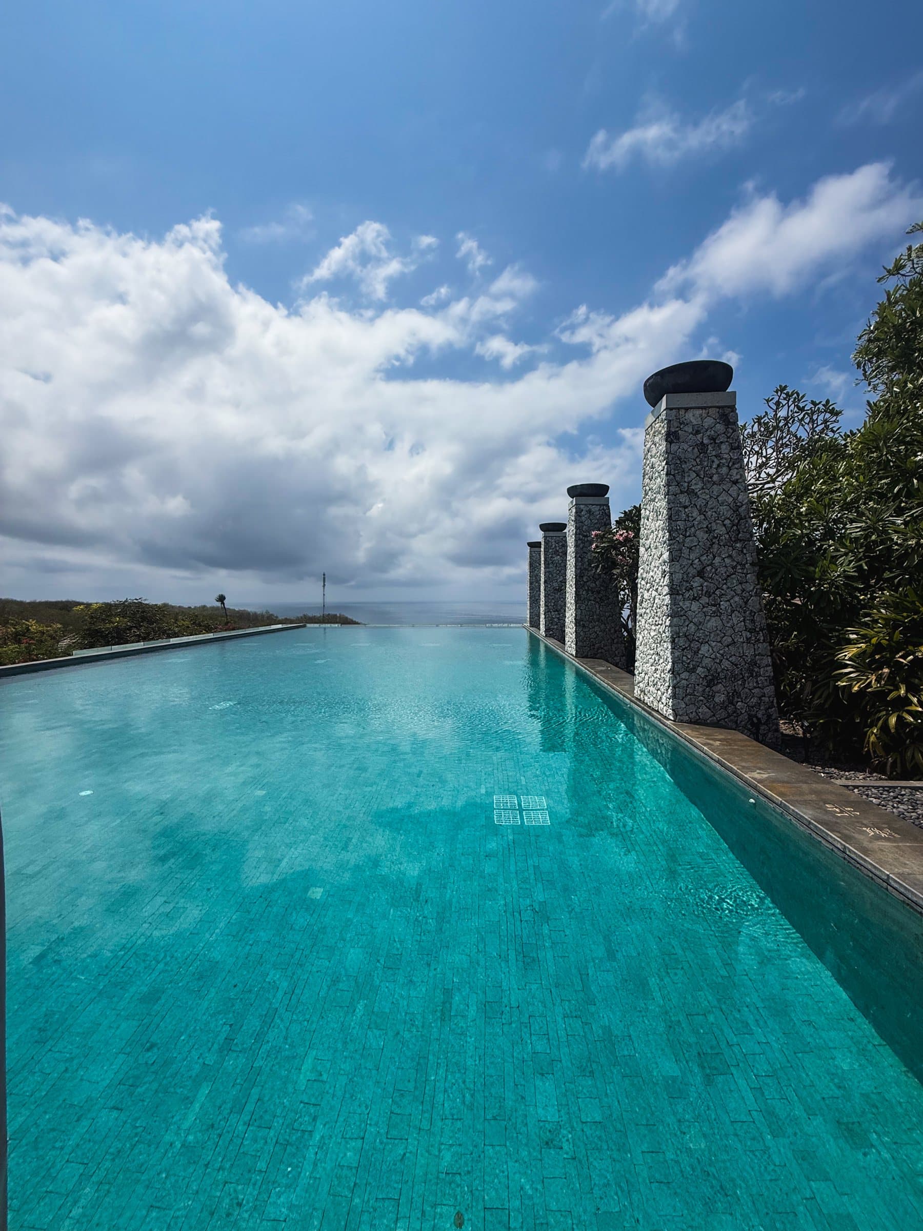 Turquoise lap pool lined with tall stone pillars under a big sky