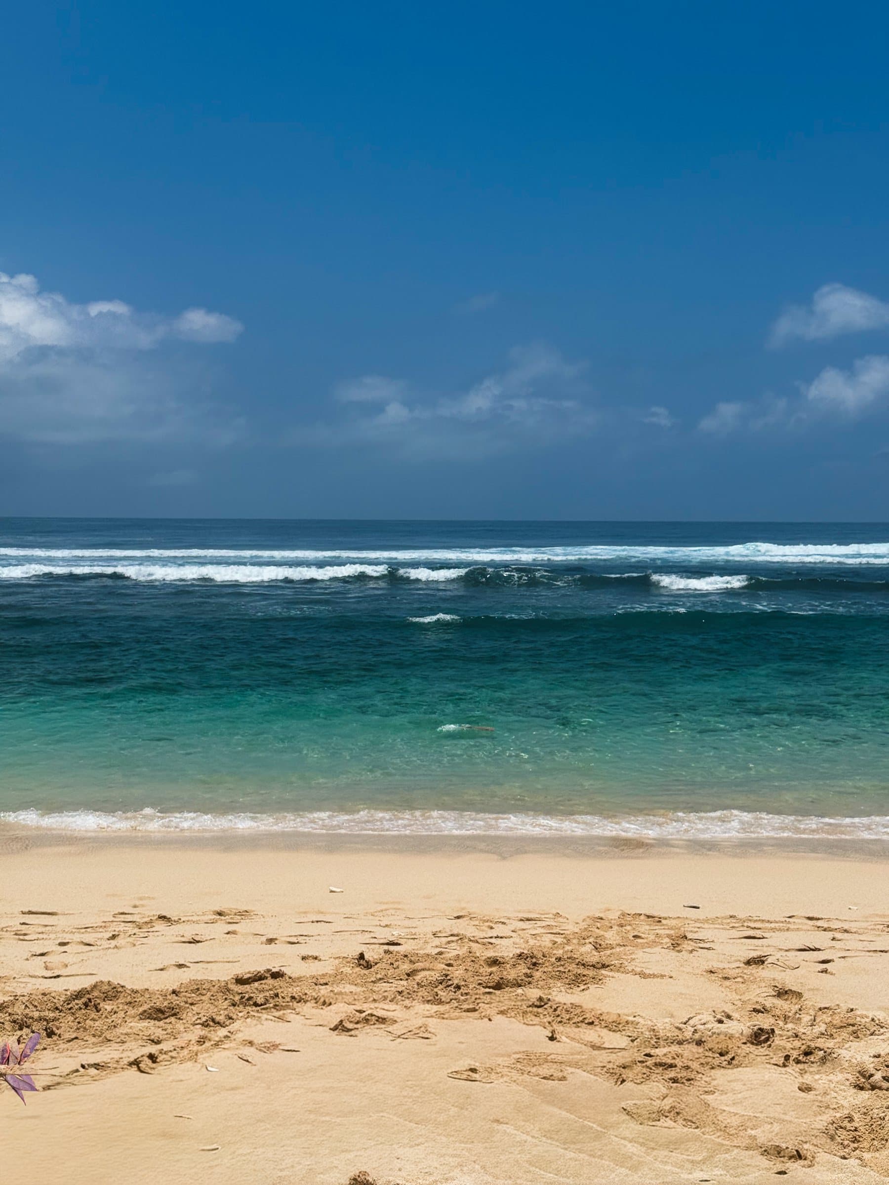 Sand beach and a line of breaking surf under a blue sky