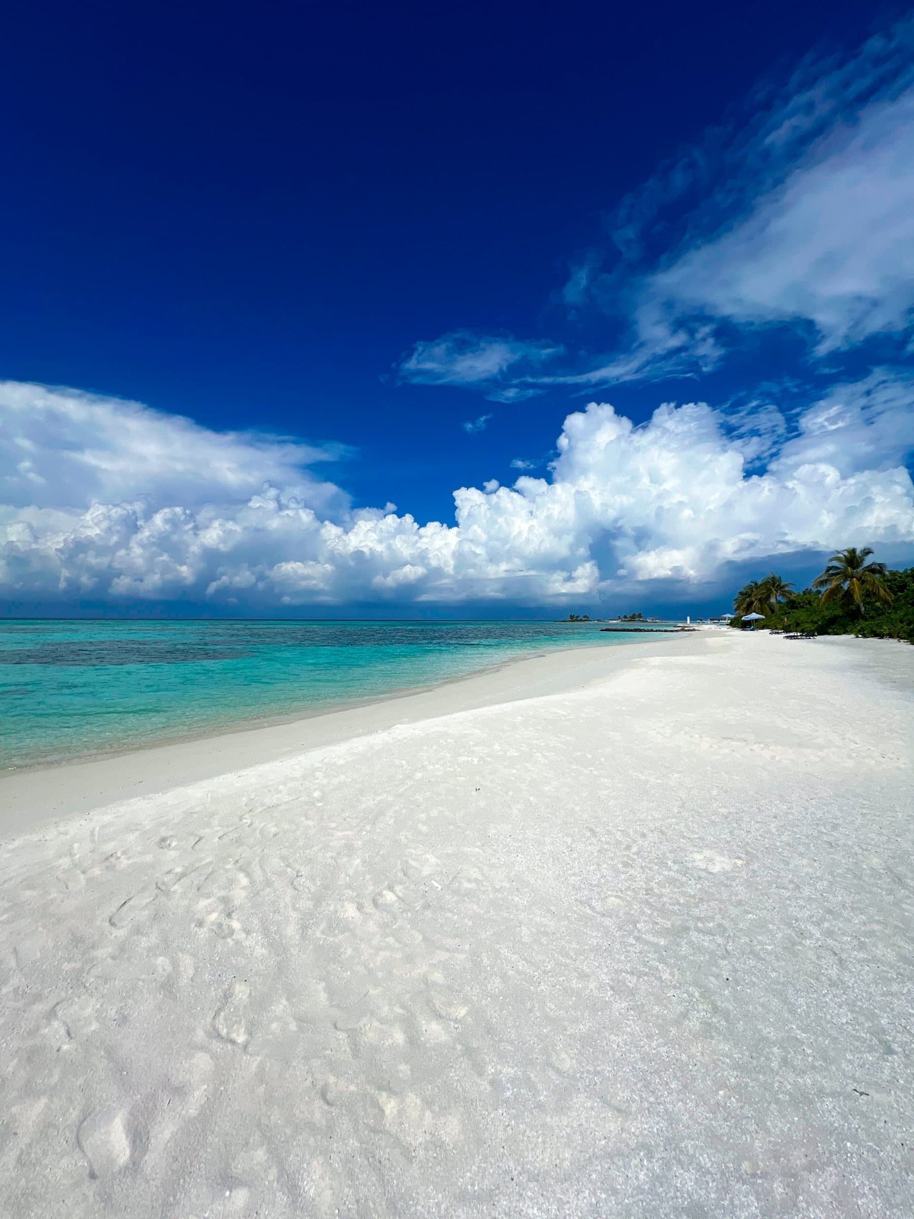 White sand shore curving into turquoise water under big clouds