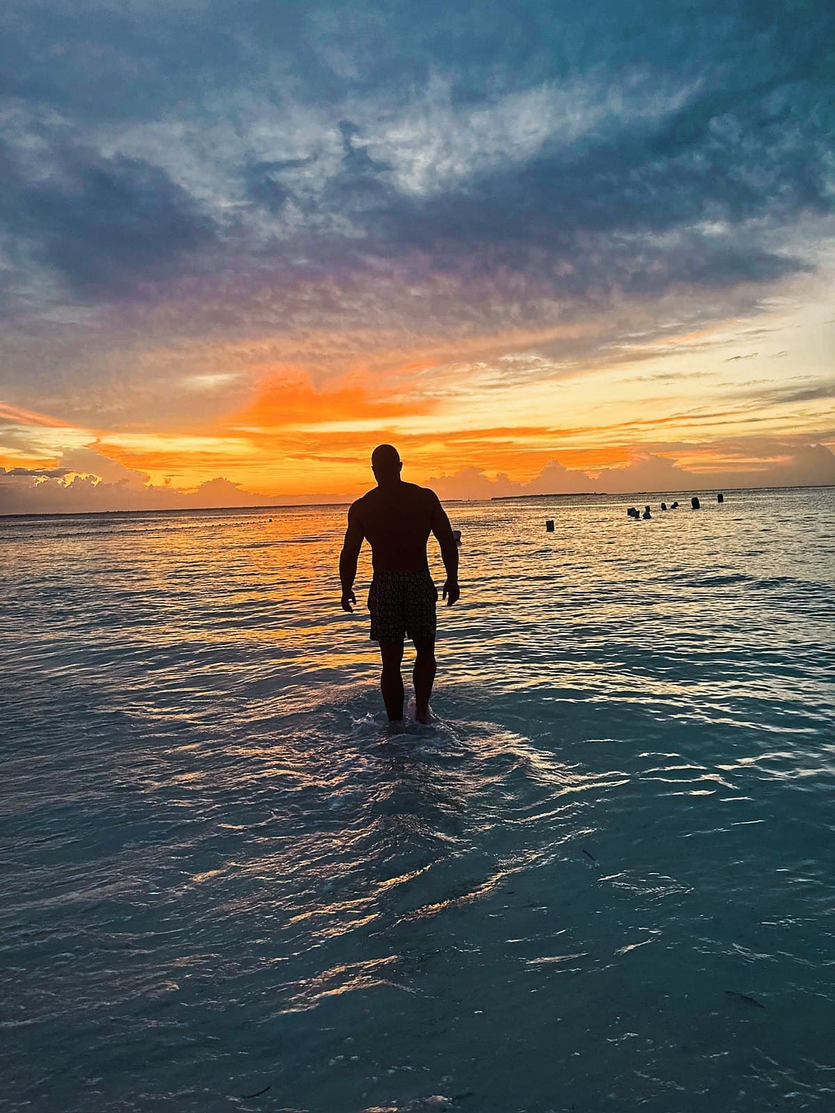 Figure wading in shallow water at sunset, back to the sky